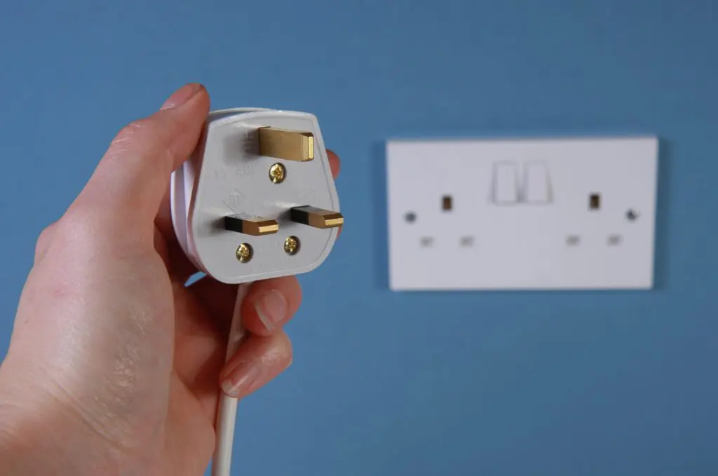 Close up of the back of a plug with a wall socket in the background