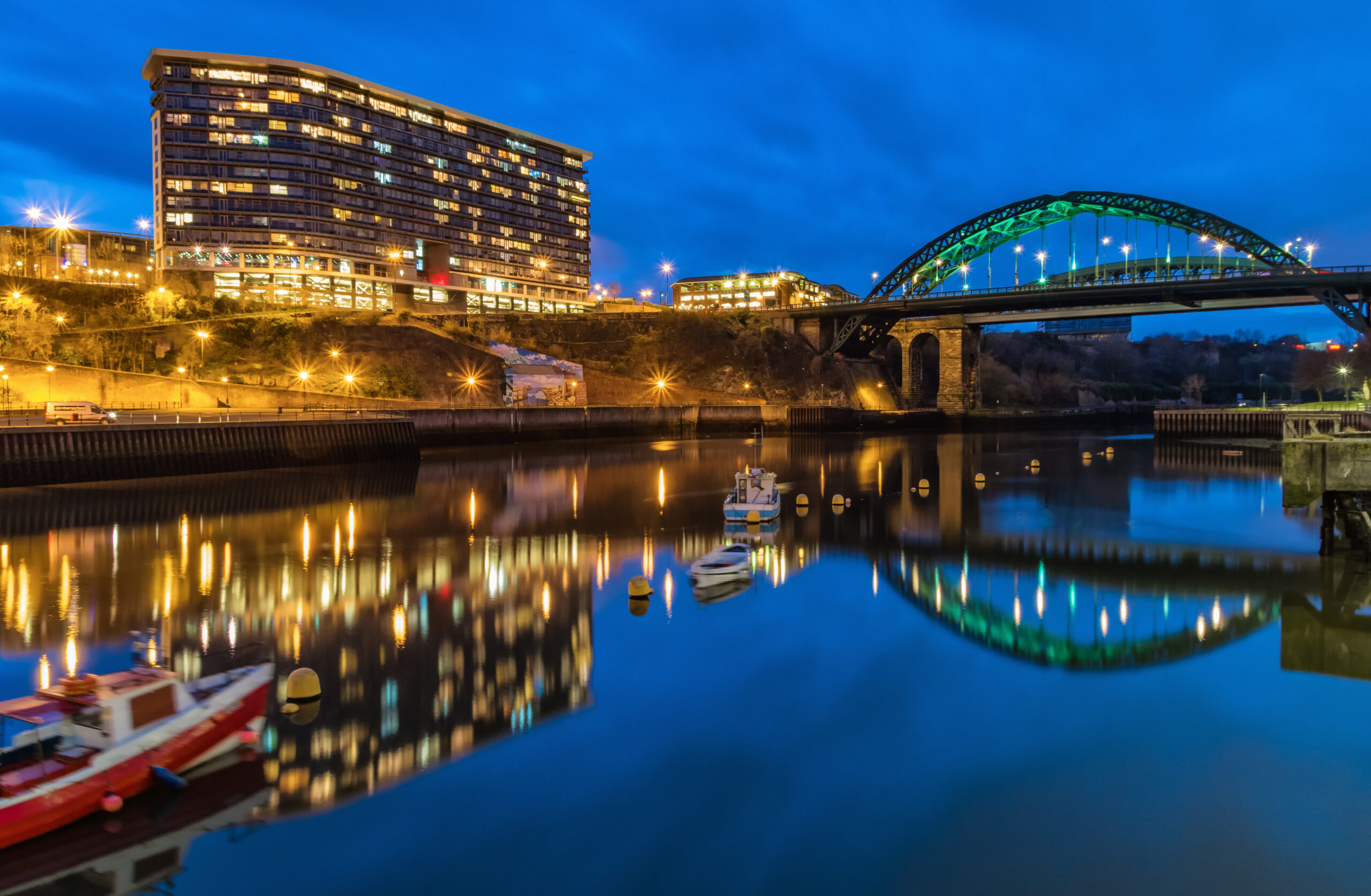 Image of a lake at nigh time with a tall office building on the side in Sunderland where we do Pat Testing